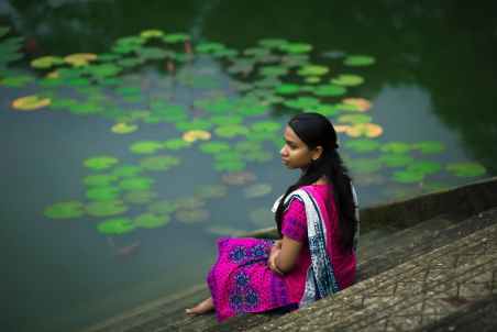 woman in pink sari dress sitting on stair beside body of water